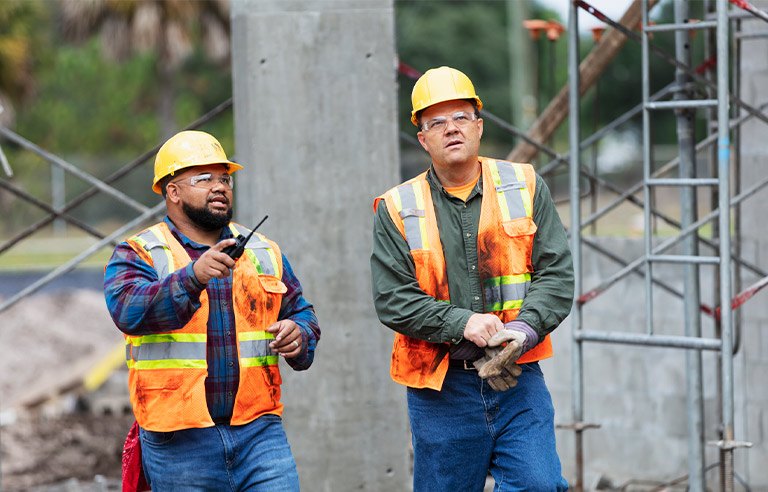 Two San Antonio construction workers in hard hats and safety vests on a job site